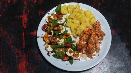Boiled potatoes, fresh salad and roasted salmon on white plate. Dark wooden background. Cuisine concept.