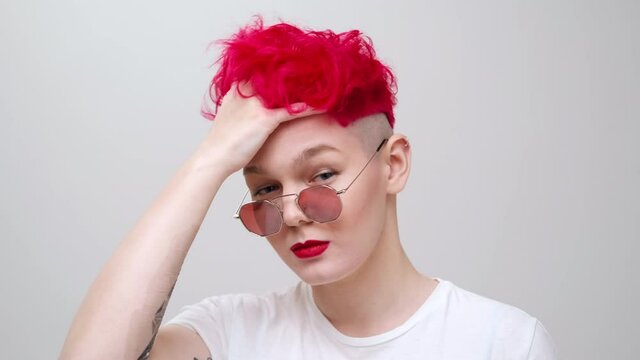 Young beautiful girl with a short bob haircut. Red colored dyed hair and sunglasses. The model poses in the studio on a white background.