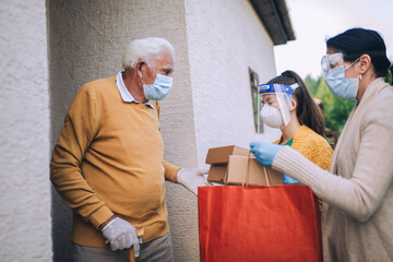 Fototapeta na wymiar Young female volunteers in mask gives an elderly man boxes with food near his house. Quarantined, isolated. Coronavirus covid-19. Donation