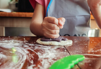 Little girl works out with a dough. Making pizza or homemade cookies. Classes during quarantine and self-isolation. Close-up of hands and dough