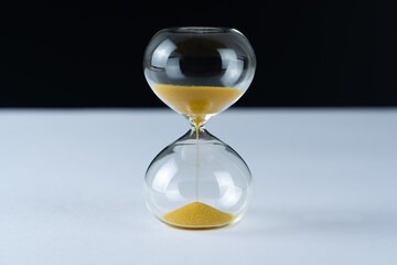 Hourglass with golden sand on a white table, black background and copy space