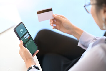 Young Asian woman holding credit card using mobile phone for internet banking and online shopping in office.
