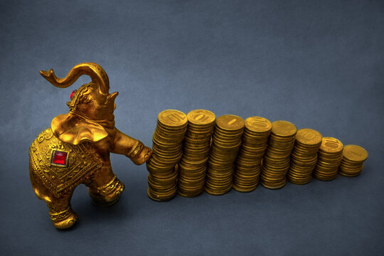 Growth and collapse of the stock market.  Gold Elephant pushes stacks of golden coins on grunge background with blank copy space.  Money is evil concept. Market saturation. Economic cycle
