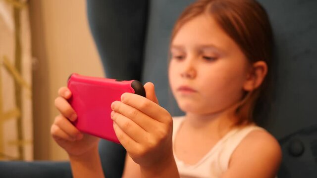 Little child girl sit in a chair hold use smartphone playing phone game application and watch social media