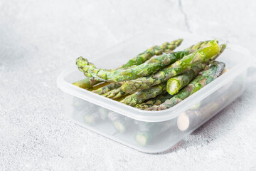 frozen green asparagus pods in a clear white container. on texture. light background. copyspace