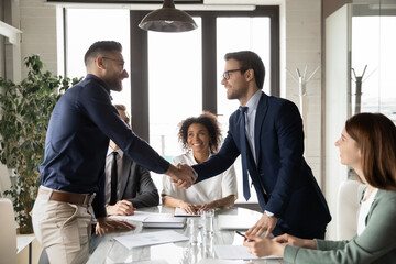 Smiling multiethnic businesspeople shake hands close deal make agreement after successful company...