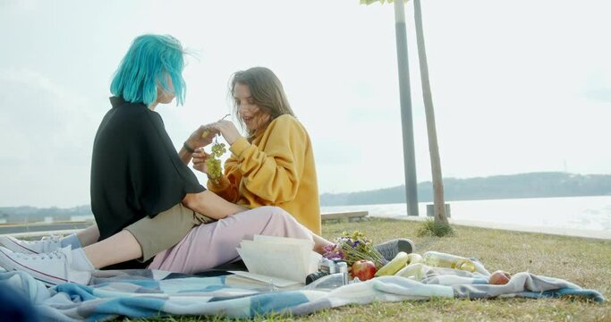 Happy young LGBT couple on a date picnic by the river in the park eating grapes and fruits romantically feeding each other