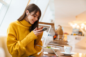 Charming happy girl taking photo on mobile phone while having lunch