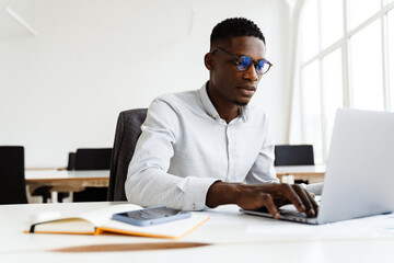Afro american focused man in eyeglasses working with laptop