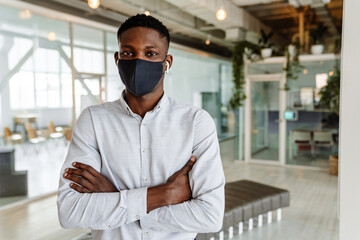 Fototapeta na wymiar Afro american young man in face mask and earphones standing indoors