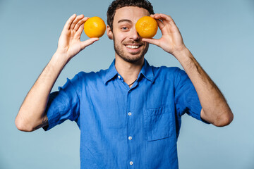 Joyful handsome guy smiling while making fun with mandarins