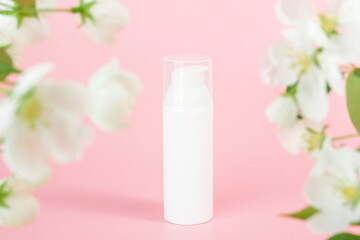 Fototapeta na wymiar White cosmetic airless dispenser. White blank cosmetics bottles and tube on glass podium and flowering branch, pink background. Natural Organic Spa Cosmetic Beauty Concept Mockup