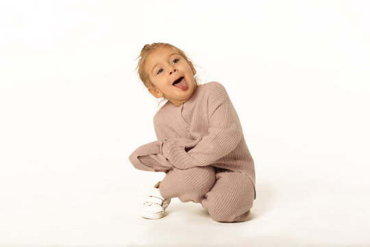 cute little blond baby girl sit the floor in pink knitted pant suit show tongue full body photo