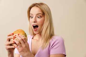 Surprised beautiful blonde girl posing with hamburger