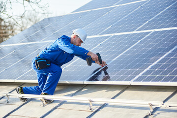 Male engineer in blue suit and protective helmet installing solar photovoltaic panel system using...