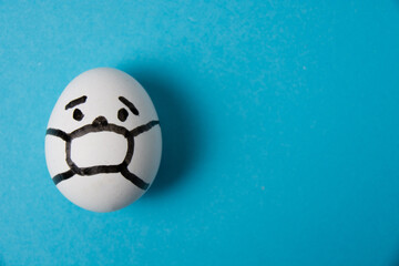 Fototapeta na wymiar An egg with a masked face. Isolate on a blue background. Covid 19 and quarantine concept