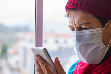 senior woman using mobile phone with mask and disposable medical gloves. Safety measures during the coronavirus outbreak