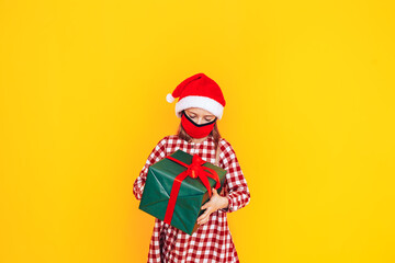 Fototapeta na wymiar Child holding large boxes with gifts. There is a Santa hat on her head, and a medical mask on her face. Christmas mood. A perfect photo for a Christmas advertisement during a pandemic