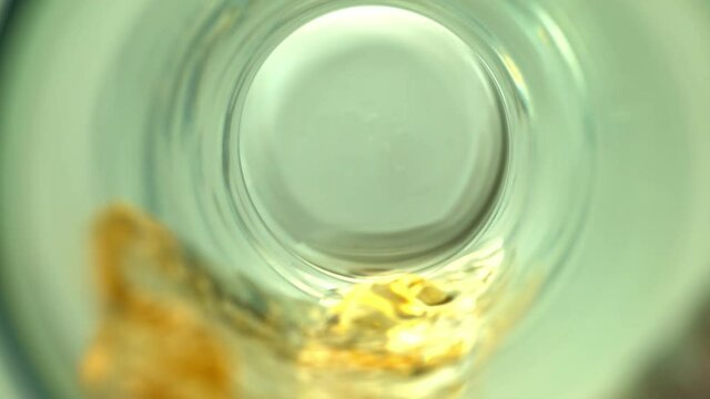 Clouse-up of a transparent glass with an orange drink pouring in it on a light gray background in slow motion, 1000fps
