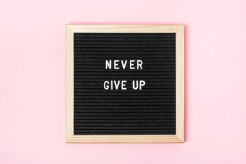 Never give up. Motivational quote on black letter board on pink background. Concept inspirational quote of the day. Greeting card, postcard