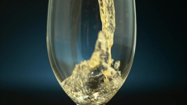 Clouse-up of a transparent glass with a drink pouring in it on a dark blue background in slow motion, 1000fps