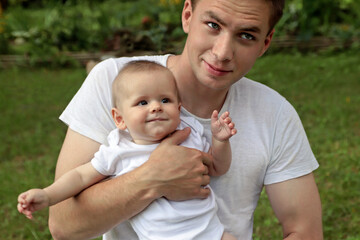 Naklejka na ściany i meble A young guy holds a baby boy in his arms and shows a gentle and warm relationship.