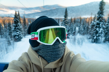 Fototapeta na wymiar guy in a protective reflective mask from the snow on the background of a picturesque mountain winter nature. Travels alone through the ski resort