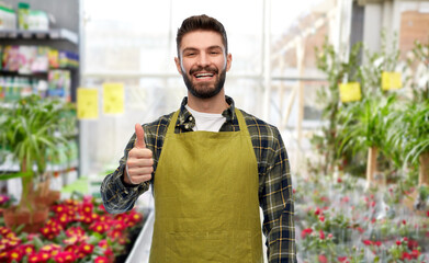 gardening, small business and sale concept - happy smiling male gardener or seller in apron showing thumbs up over flower shop background