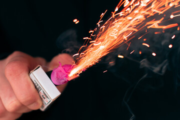 The Firecracker in a Hand. Man Holding a Burning Petard in His Hand. A Human with a Pyrotechnics that Burns with Sparks and Smoke Outdoors