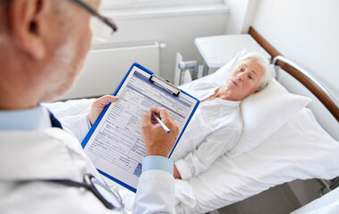 medicine, healthcare and people concept - senior woman and doctor writing to clipboard at hospital ward