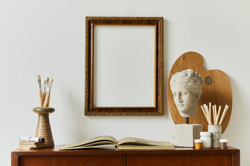 Stylish composition of artist workspace room with design retro teak commode, mock up poster frame, book, decoration and painting accessories. Template.