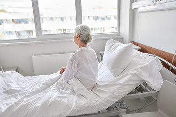 Obraz premium medicine, healthcare and people concept - lonely senior woman sitting in bed at hospital ward