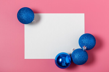 Blue Christmas balls and white blank paper with copy space on a pink background. christmas and new year celebration concept. flat lay, mockup, top view, minimalism.