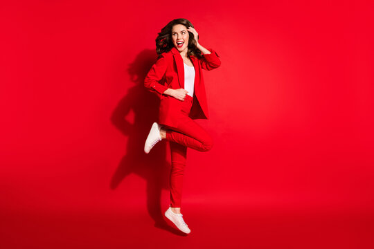 Full length profile photo of pretty young lady jump look empty space wear jacket pants sneakers isolated red color background