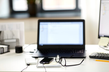 business, work and interior concept - laptop computer, smartphone, glasses and stationary on table at office