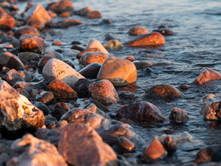 Rocks and pebbles on the beach being watered as the waves wash in on the beach at sunset