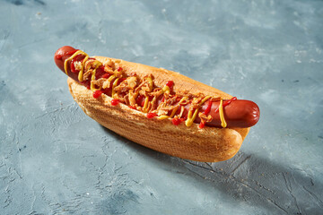 Classic hot dog with sausage, ketchup, mustard and fried onions in a white bun on a gray...