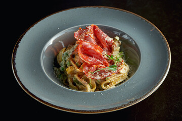 Italian pasta with chanterelle mushrooms and chorizo, parmesan cheese in a gray plate on a black background. Close up