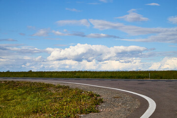 Beautiful landscape with blue sky, white clouds and the road that goes to the horizon through field.