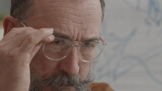 Close-up of smart experienced Caucasian man with silver mustache and beard looking carefully at invisible thing, taking off and putting on glasses