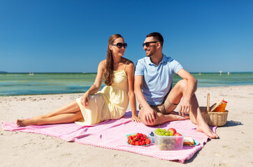 leisure, relationships and people concept - happy couple in sunglasses having picnic on summer beach