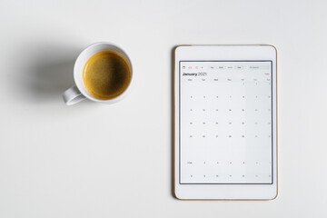 Minimal calendar flat lay. Digital tablet with open 2021 calendar app and cup of coffee on white background. Planning next new year.