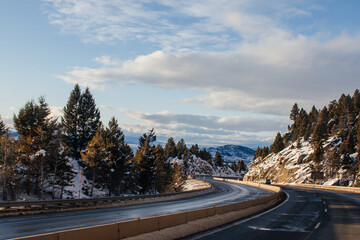 Highway in beautiful place in winer on the summer day. Landscape with asphalt road, trees, snow-covered mountain in winter. Montana, USA, 12-2-2019