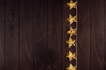Youth stylish decoration for party - golden stars lights on dark wood board, border, top view.