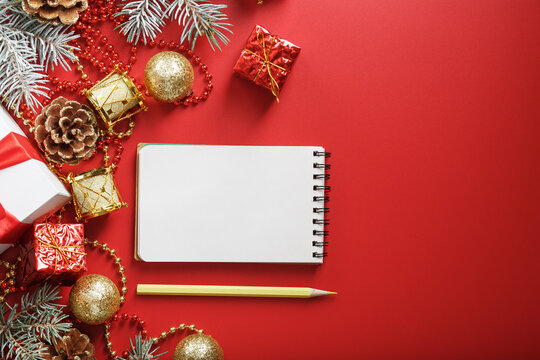 Christmas composition with notepad and a pencil for writing wishes with Christmas tree decorations on a red background.