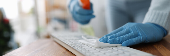 Female hands in rubber gloves wiping keyboard with antiseptic napkin in office. Disinfection of...