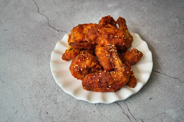 Deep fried chicken wings and drummets coated with hot and spicy Korean sauce on a white plate and green cloth.