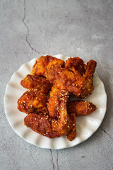 Deep fried chicken wings and drummets coated with hot and spicy Korean sauce on a white plate and green cloth.