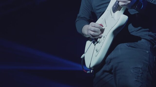 Close-up shot of a man's hand playing an electric guitar on stage. Six-string guitar. The guitarist in black performs on stage, rock music concert. 