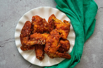 Deep fried chicken wings and drummets coated with hot and spicy Korean sauce on a white plate and green cloth.